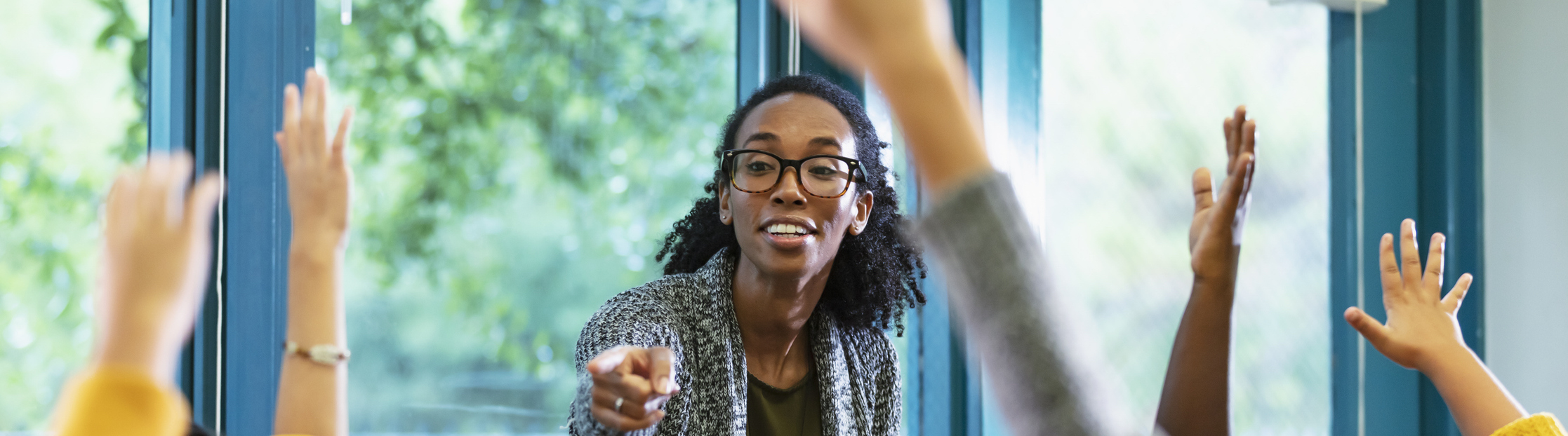 Teacher in classroom points to student raising hand